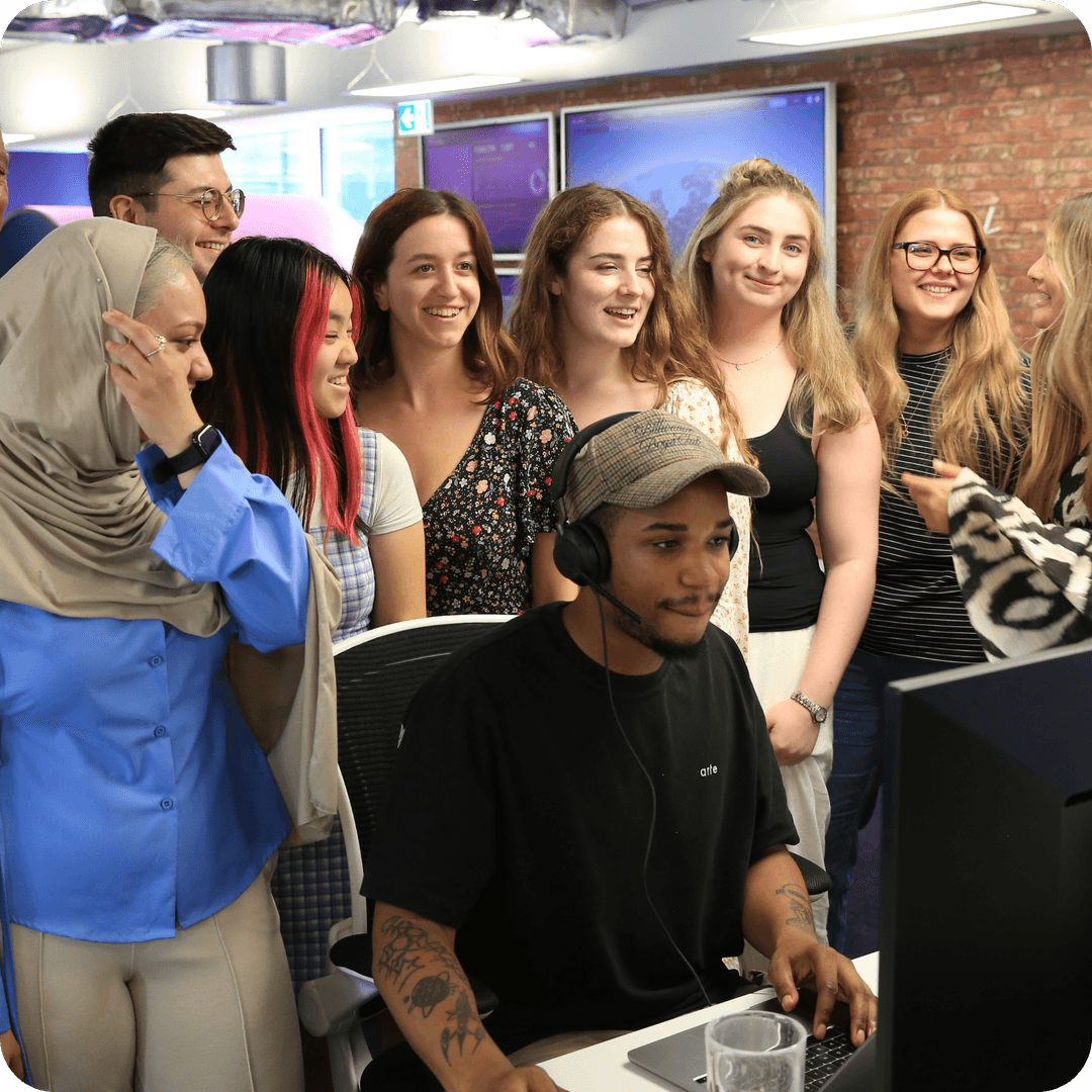 A group of smiling young people in an office in front of a computer
