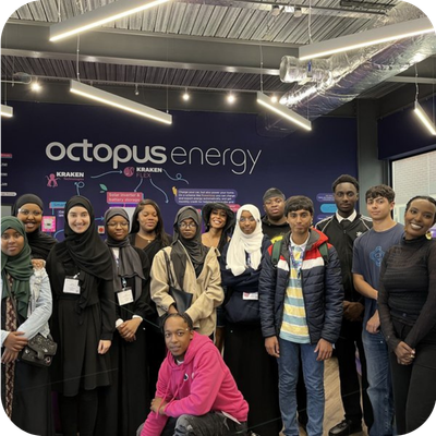 Group of young people inside Octopus Energy office, standing and smiling, with a company logo on the wall behind them.